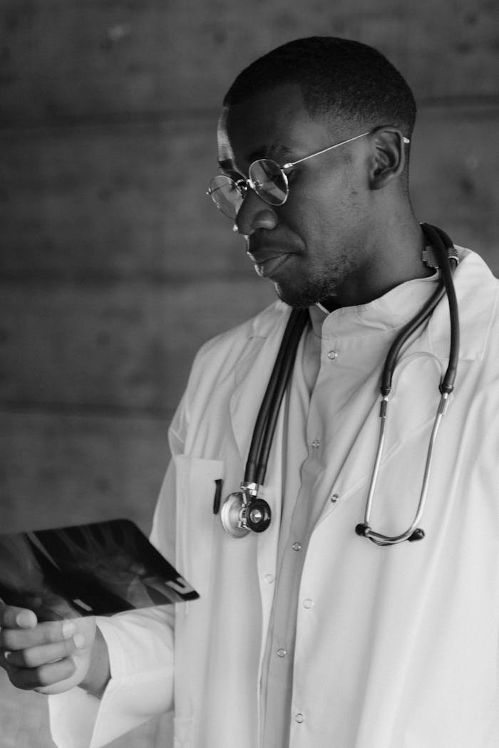 Monochrome image of a doctor examining an X-ray, wearing a stethoscope and lab coat.